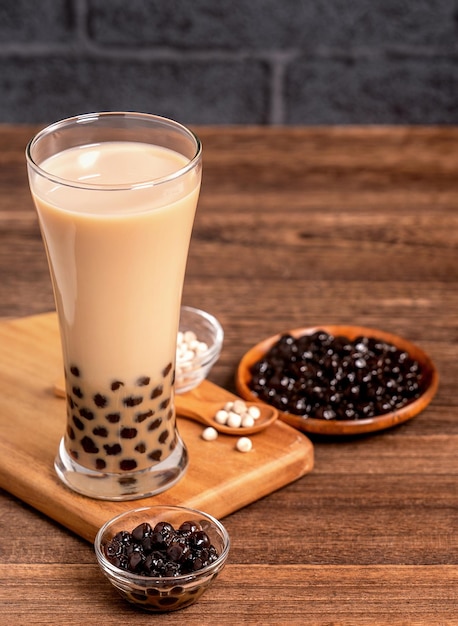 Delicious bubble milk tea with tapioca pearl ball in glass on wooden table and dark gray brick background popular food and drink in Taiwan close up