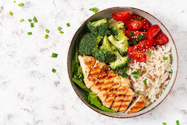 Delicious buddha bowl with grilled chicken fresh vegetables and rice on a light background Top view above