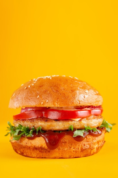 Delicious burger with greens and red bell peppers on a yellow background. Tasty fresh unhealthy burgers with cheese and two patties. Fast food, unhealthy food concept.