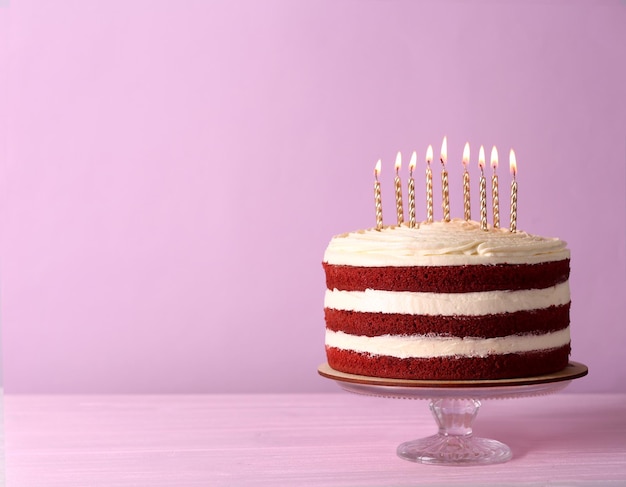 Delicious cake with candles on pink background