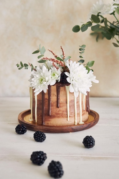 Delicious cake with white and brown chocolate swirly with flowers and blackberries on a table