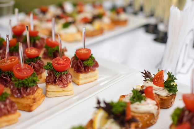 Delicious canape with sausage and tomato.Canapes on white ceramic plates at wedding reception.