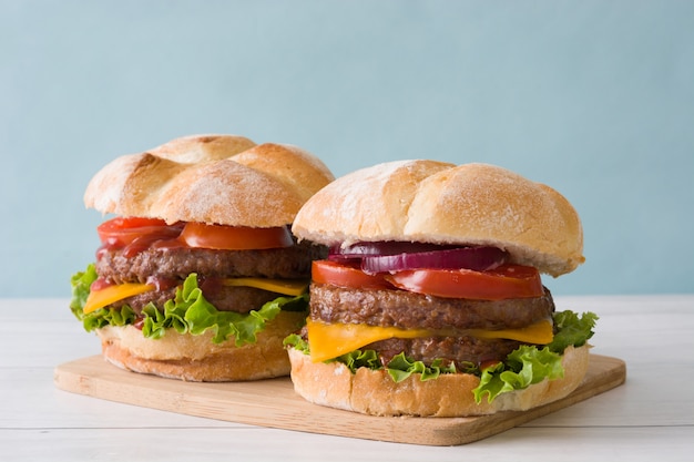 Delicious cheeseburgers and vegetables on white wooden table and blue