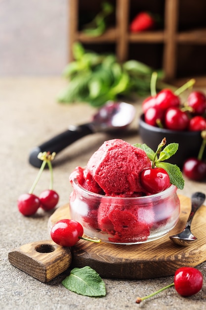 Delicious cherry ice cream in a glass bowl with fresh cherries on wooden cutting board