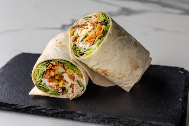 Delicious chicken wrap served on a black board on the marble table