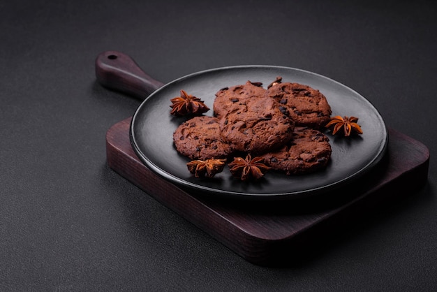 Delicious chocolate cookies with nuts on a black ceramic plate on a dark concrete background