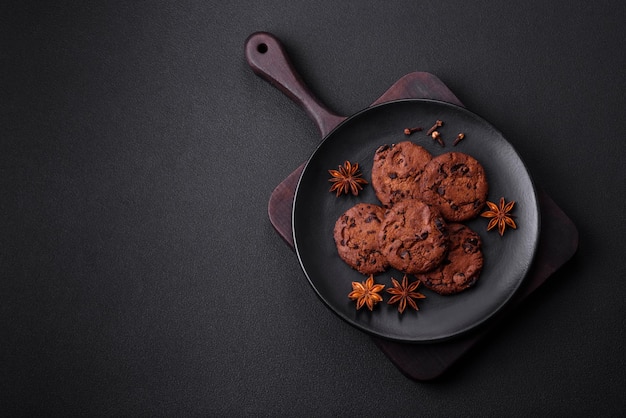 Delicious chocolate cookies with nuts on a black ceramic plate on a dark concrete background