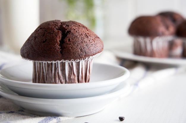 Delicious chocolate muffins in paper cups on a plate on white background