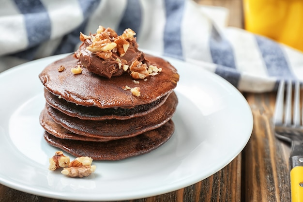 Delicious chocolate pancakes decorated with nuts on plate