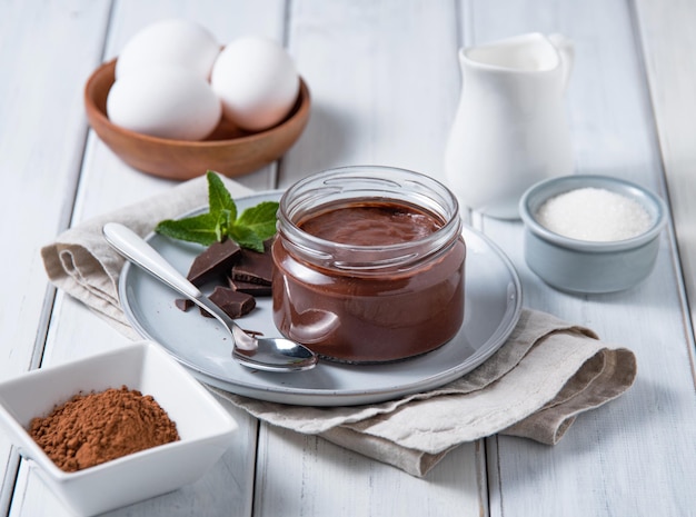 Delicious chocolate pudding in a jar on a light wooden background with ingredients The concept of homemade healthy chocolate mousse