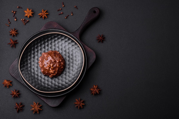 Delicious chocolate tart with nuts on a black ceramic plate on a dark concrete background