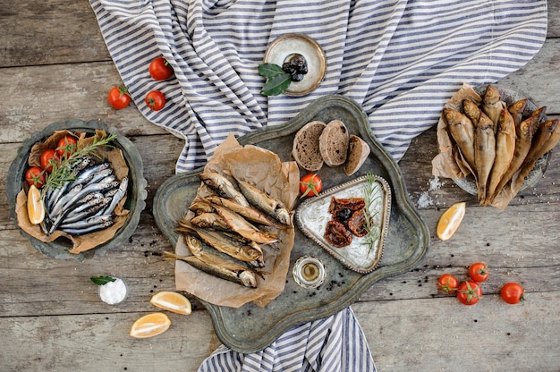 Delicious composition on the wooden table and grey striped napkin of the smoke-dried horse mackerel and anchovies with a tomatoes, rosemary, lemon, bread and other tasty products.