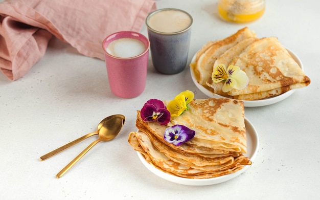 Delicious crepes on plates, decorated with flowers and coffee mugs