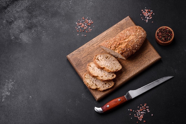 Delicious crispy bread with cereals cut into slices on a wooden cutting board on a dark concrete background