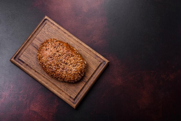 Delicious crispy bread with cereals on a wooden cutting board on a dark concrete background