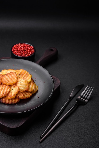 Delicious crispy fried potatoes in slices on a black ceramic plate