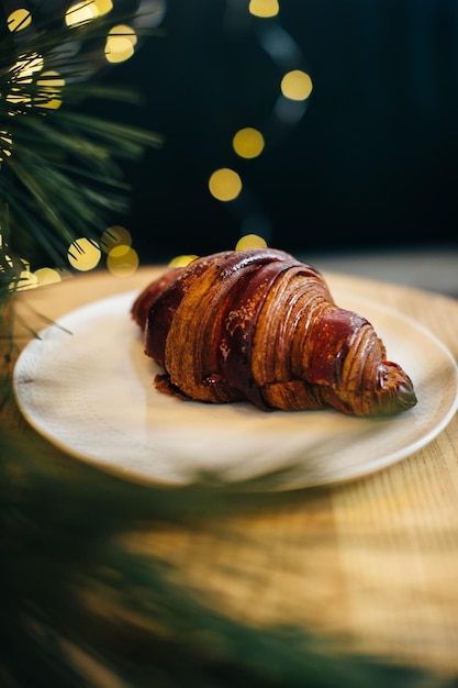 A delicious croissant on a table in a coffee shop decorated with festive Christmas lights