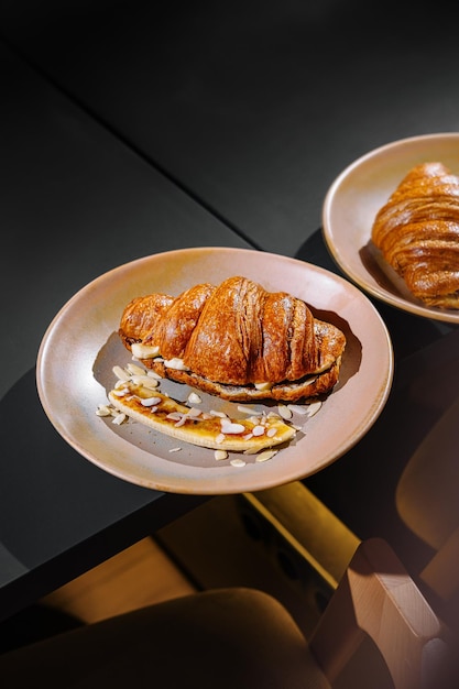 Photo delicious croissants with banana and almonds on plates on a table