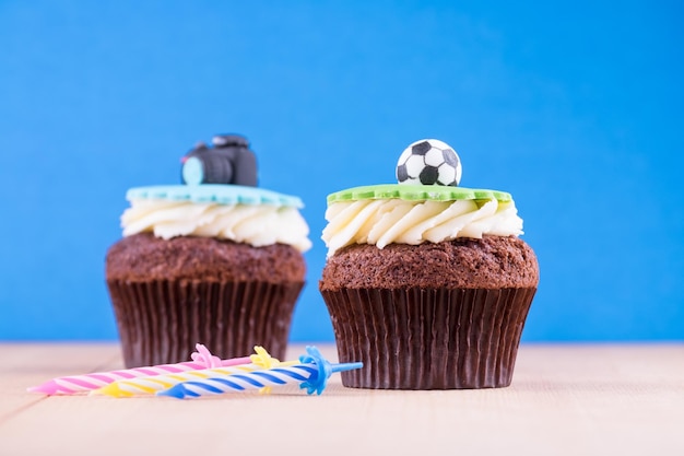 Delicious cupcakes with icons of ball and camera on it on wooden desk and blue background