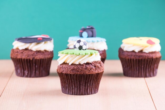 Delicious cupcakes with icons of ball tuxedo smiley and camera on it on wooden desk and green background