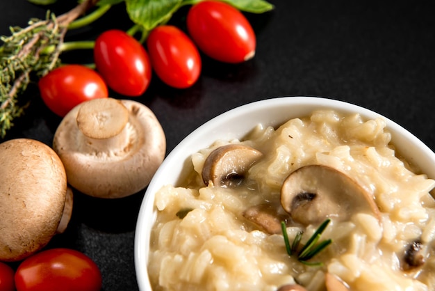 Delicious dish of Mushroom risotto on black background cherry tomatoes and herbs on black background close up