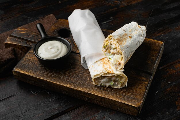 Photo a delicious doner doner kebab wrap with meat lettuce tomato red onion on cutting board on old dark wooden table background