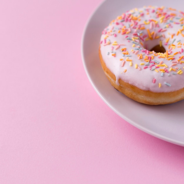 Delicious donut with sprinkles on plate at pink table.