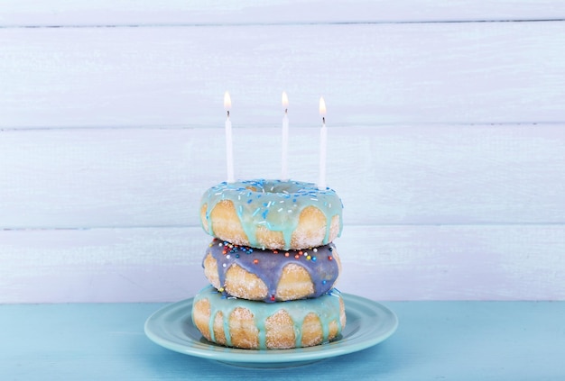 Delicious donuts with icing and birthday candles on table on wooden background