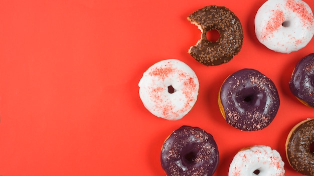 Delicious doughnuts with icing and missing bite on red background