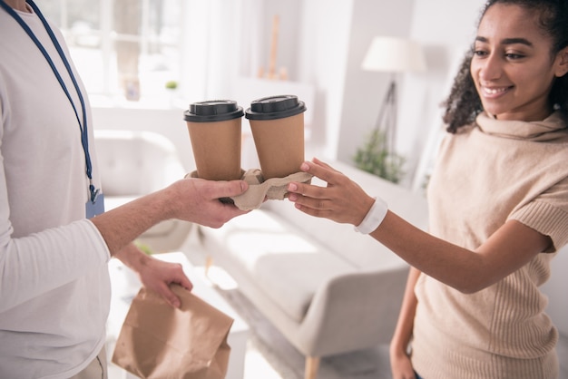 Delicious drink. Close up of cups with coffee being given to a cheerful young woman