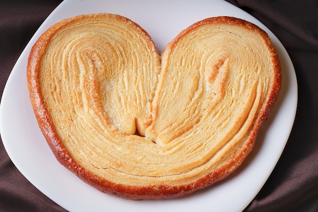 Delicious earshaped puff pastry bread with sugar on a white ceramic homemade plate