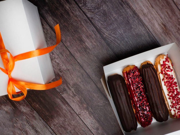 Delicious eclairs in a white box on wooden surface