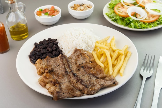 Delicious executive dish of beef steak rice beans french fries and green salad with lettuce tomato and onion accompanied by farofa and vinaigrette Typical Brazilian food Selective focus