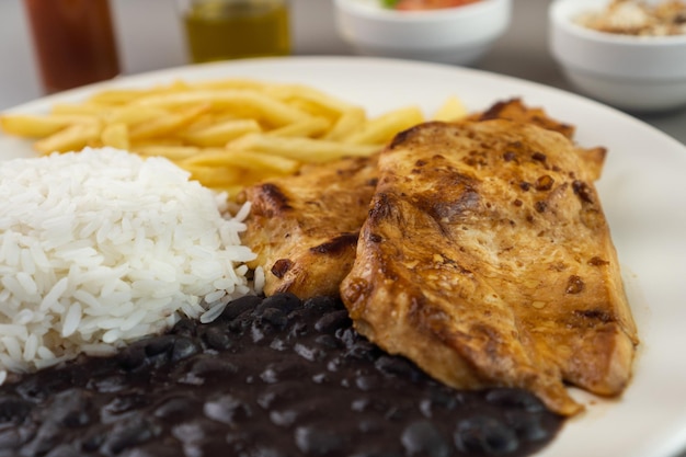 Delicious executive dish of chicken fillet rice beans french fries and green salad with lettuce tomato and onion accompanied by farofa and vinaigrette Typical Brazilian food Selective focus