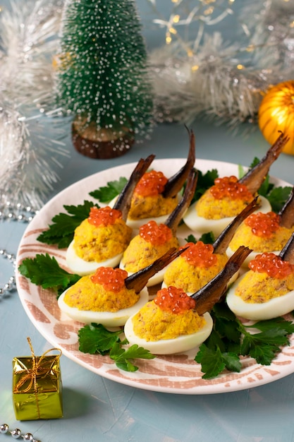 Delicious festive snack Eggs stuffed with sprats and red caviar on a plate on New year blue background