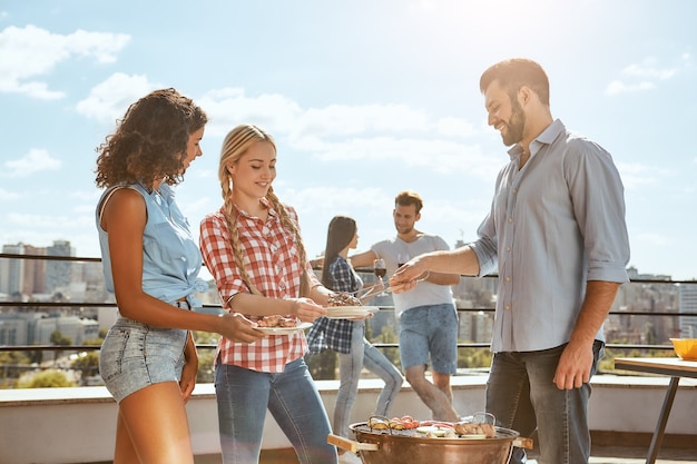 Delicious food for best friends young and cheerful man is putting hot barbecued meat on