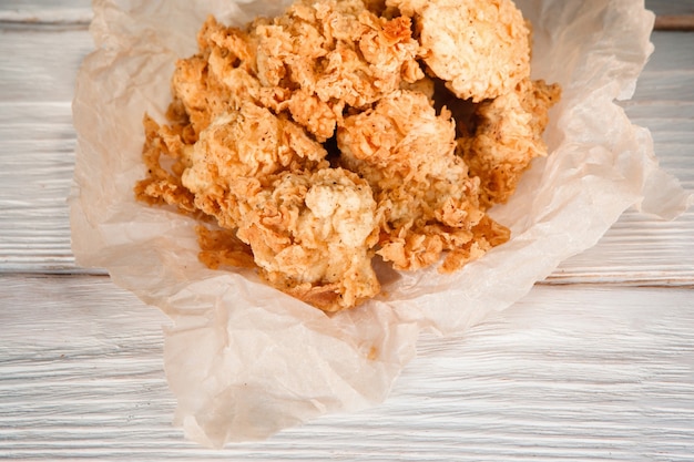 Delicious fresh baked chicken fillet on white paper, on wooden table, closeup view. Fried nuggets breaded with corn flake crumbs, beer snack, fast food. American cuisine.