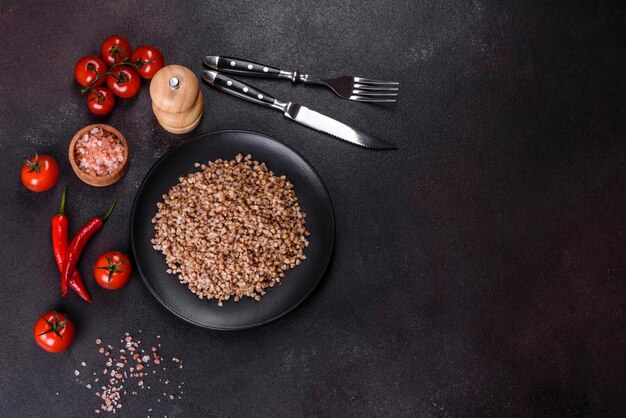 Delicious fresh boiled buckwheat porridge with vegetables and spices on a black plate