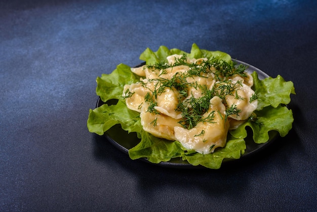 Delicious fresh cooked dumplings with potatoes embellished with greens and lettuce leaves on a dark plate