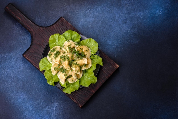 Delicious fresh cooked dumplings with potatoes embellished with greens and lettuce leaves on a dark plate