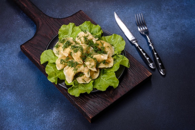 Delicious fresh cooked dumplings with potatoes embellished with greens and lettuce leaves on a dark plate