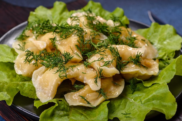 Delicious fresh cooked dumplings with potatoes embellished with greens and lettuce leaves on a dark plate