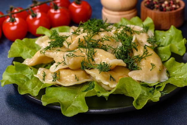 Delicious fresh cooked dumplings with potatoes embellished with greens and lettuce leaves on a dark plate