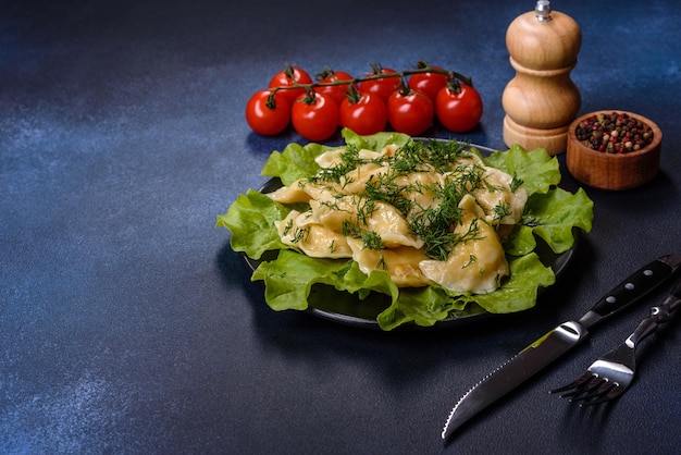 Delicious fresh cooked dumplings with potatoes embellished with greens and lettuce leaves on a dark plate