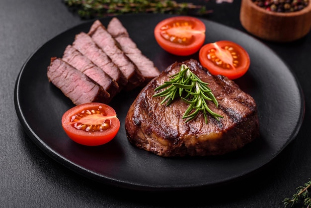 Delicious fresh juicy beef steak with spices and herbs on a dark concrete background