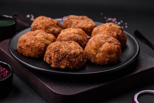 Delicious fresh meat or vegetable cutlets with spices and herbs on a black plate on a dark concrete background