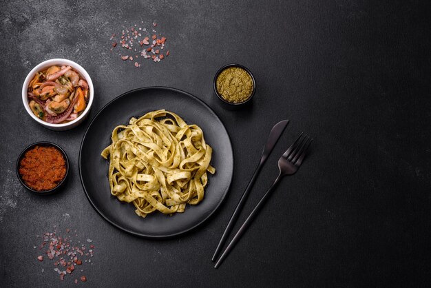 Delicious fresh pasta with pesto sauce and seafood on a black plate