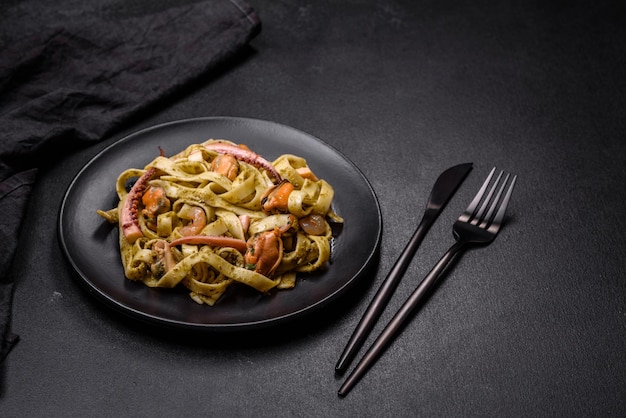 Delicious fresh pasta with pesto sauce and seafood on a black plate