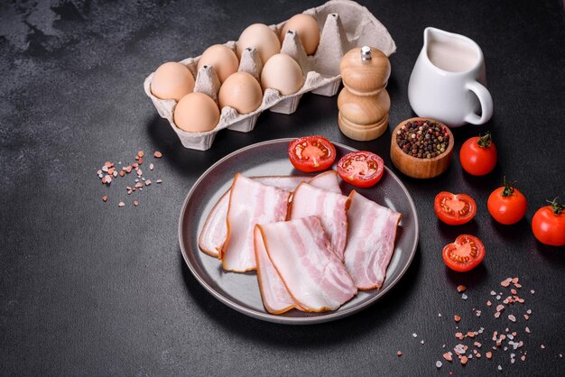 Delicious fresh raw bacon cut with slices on a grey plate against a dark concrete background