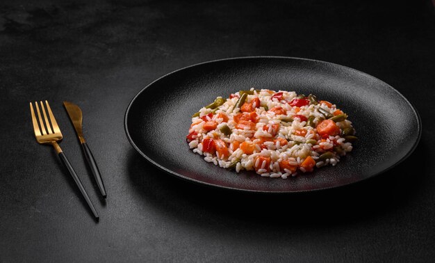 Delicious fresh risotto with vegetables spices and herbs on a black plate on a dark concrete background